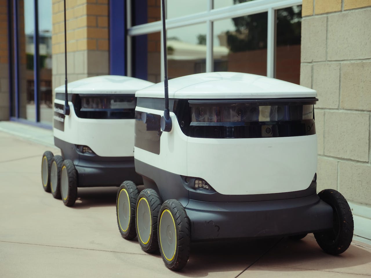 Two autonomous delivery robots positioned outside a modern building, showcasing innovation in robotics and mobility.